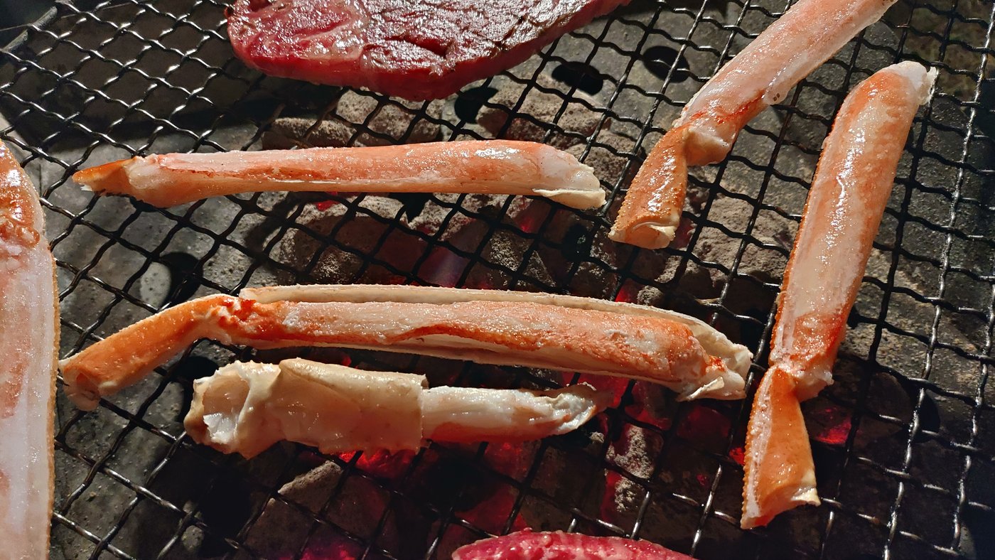 炭火の網で焼くカニの脚とステーキ